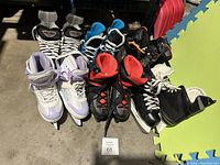 Five pairs of children's ice skates of various colors and sizes shown together on a floor, some with visible laces and ankle straps