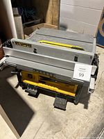 Side angle of the DeWalt table saw showing the metal work surface, yellow blade slot cover, and black frame legs with dust collection port.