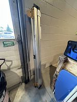 Full view of DeWalt folding metal work stand in folded position leaning against wall.