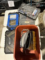 Overview photo showing multiple plastic cases with drill bits, black carrying case, small zippered pouch, and plastic organizer boxes inside a red bin