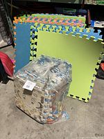 Foam mats including large solid color pieces and a sealed bundle of smaller animal print mats, shown in a storage area.