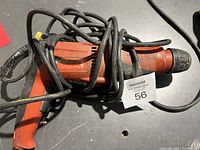 Overall view of the orange Hilti electric drill coiled with black power cord on a black surface.