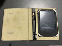 Open view of the Kobo e-reader inside the worn black protective case with a pen in holder, e-reader screen showing charge prompt.