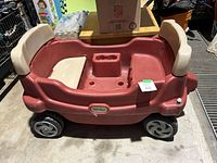 Photo showing the side view of the red plastic wagon with beige bench seats, cupholder in the middle, and two front wheels visible.