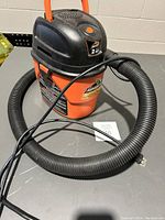 Front-side view of Armor All portable shop vacuum on gray surface with flexible hose and power cord coiled on top.