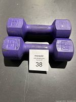 Pair of purple hexagonal 5lb hand weights shown from above on a dark surface, featuring a textured grip handle and minor scuff marks.