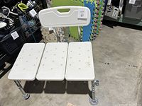 White plastic 3-panel shower safety seat with adjustable aluminum legs and suction cups shown from front side with visible backrest.