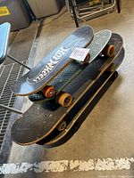 Stacked view of several skateboards showing varying deck sizes and wheel colors, wear visible on decks and wheels