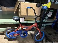 Full side view of red Spiderman themed kids bike with blue rims and pedals, yellow horn on handlebar.