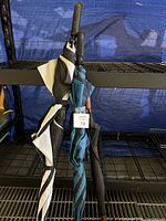 Three sport-sized umbrellas, black and white patterned, blue with black stripes, and solid black, shown standing together with tags.