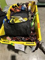 Yellow plastic container holding mixed tie-down and ratchet straps, visible ratchet handles, hooks, and storage bag.
