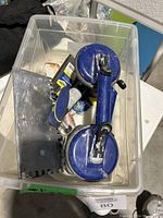 Photo showing the blue double suction cup lifter, black grout sponge float, notched trowel, and other tiling tools inside a clear plastic container.