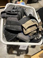 Photo showing a plastic bin filled with various tool belts including black fabric and brown leather types, visibly dirty and worn.