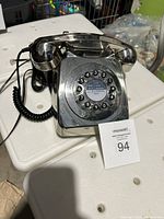 Front view of the vintage style rotary dial phone showing the rotary dial, handset resting on the cradle, coiled cord, and chrome reflective finish.