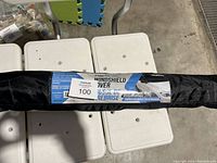 Folded windshield protector cover in its carrying pouch on white foam surface with label visible stating use for cars, trucks, SUVs, and protection for wipers and windshield.