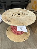 Front view of red insulated wire wound on a wooden spool showing dirt and wear on the wooden surface.