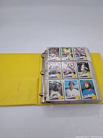Yellow three-ring binder opened to show nine baseball cards in clear plastic sleeve, featuring players from various teams and backgrounds.