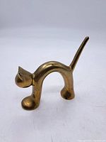 Photo of brass cat paperweight viewed from side showing arched back and elongated tail raised vertically.