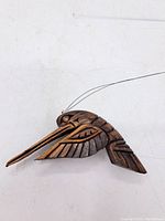 Front view of the carved wooden hummingbird showing its long beak, detailed wings, and wire attached for hanging.