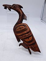 Full front view of carved wooden crane standing, showing stylized patterns and fish in beak