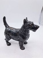 Front left angle view of the black cast iron Scottie dog figurine, showing general wear and detail of texture.