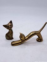 Both brass cat paperweights together, showing seated and stretching cat figurines with brass finish and some wear.