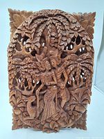 Front view of the carved wooden panel showing two human figures under a leafy tree with an animal figure at the bottom.
