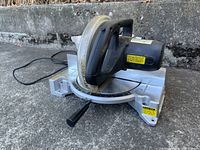 Miter saw placed on pavement showing front angle with handle and base.