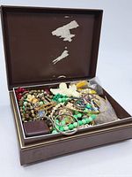Brown jewelry box filled with assorted vintage costume jewelry including various necklaces, bracelets, and earrings.