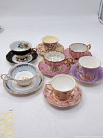 Image showing set of seven assorted tea cups with matching saucers in various floral and pastel designs on white background.