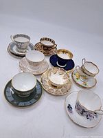 Image showing all nine assorted tea cups with matching saucers arranged for visibility. The variety of colors and patterns is clear, including floral, geometric, and gold accent designs.