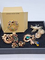 Image showing all assorted costume jewelry pieces on black background including Jones New York brooch in box and various pins and earrings.