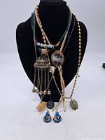 Multiple necklaces displayed on a black velvet bust showing various pendants and chains.