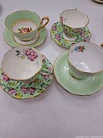 Photo showing four vintage bone china tea cups and matching saucers with floral and pastel designs and gold rims