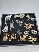 Full view of all 12 assorted vintage brooches arranged in a display box showing various designs and metal tones.