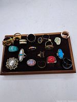 Overview of 17 assorted vintage rings on brown velvet tray showing various sizes, colors, and materials.