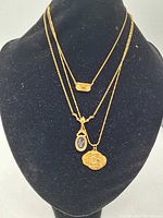 Three gold-tone zodiac sign necklaces displayed on black jewelry bust. Pendants include a crab, a scorpion cameo, and a small bar with zodiac engraving.