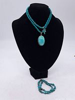 Two turquoise necklaces displayed on black bust and turquoise chip bracelet laid below.