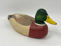 Side view of painted wooden mallard duck decoy showing green head, yellow beak, red chest, beige body and detailed wing and tail feather paint.
