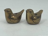 Pair of small brass bird candle holders side by side showing front and wing detail.
