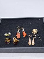 Overview of all earrings and vintage stickpin arranged on black felt display.