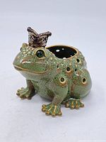 Side view of green frog candle holder with metallic crown and multiple holes on body
