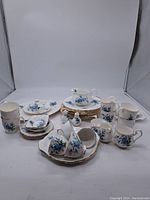 Full set of Royal Albert Forget-Me-Not dinnerware pieces including plates, bowls, cups, saucers, creamer, sugar bowl, and salt and pepper shakers arranged and visible.