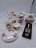 Full set displayed including teapot, six teacups and saucers, six side plates, creamer, sugar bowl, and cake server in box with floral handle.
