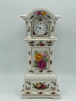Front view of Royal Albert bone china clock showing the face with Roman numerals, floral decals, and sculpted roses in pink, yellow and red on white china with gold trim.