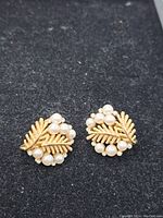 Front view showing gold-tone textured leaf design with clusters of faux pearls on dark background.