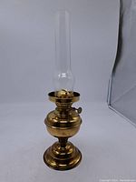 Full view of vintage brass oil lamp showing the base, reservoir, and glass chimney standing upright.