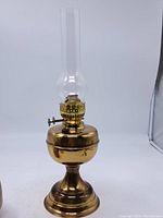 Full view of the vintage brass oil lamp showing bulbous brass base, stem, and glass chimney with wick adjustment mechanism.