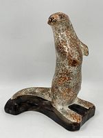 Front view of vintage glazed ceramic otter figurine standing on a dark curved base showing mottled brown and white glaze finish.