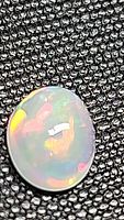 Close-up photo of oval cabochon Ethiopian opal with strong multi-color flash on textured black background